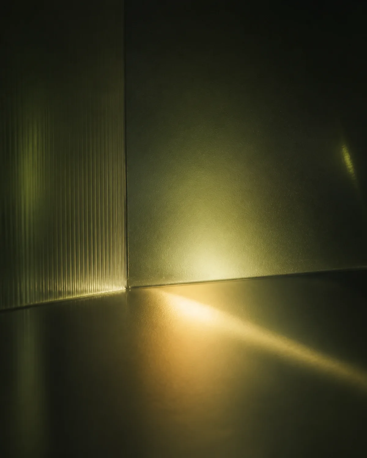A single shaft of warm light crossing a dark green pane of ribbed glass