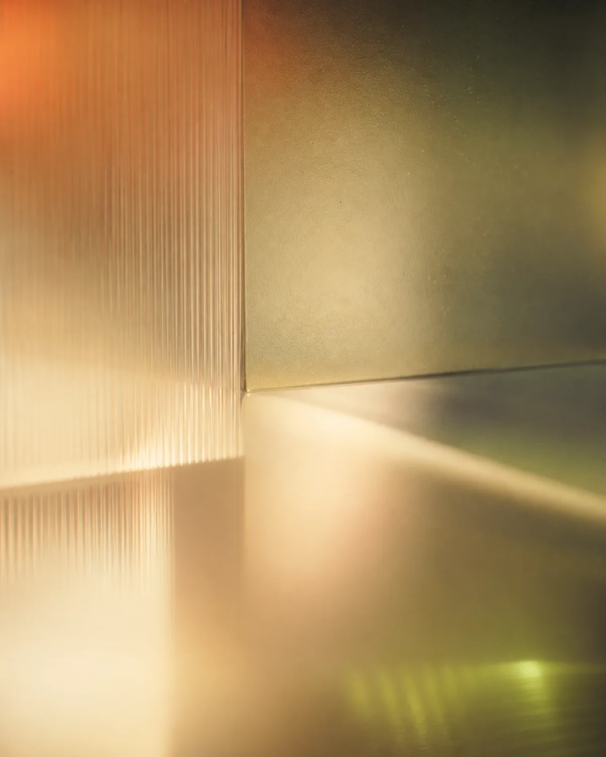 Warm amber light falling across a pane of ribbed glass and a brushed metal edge