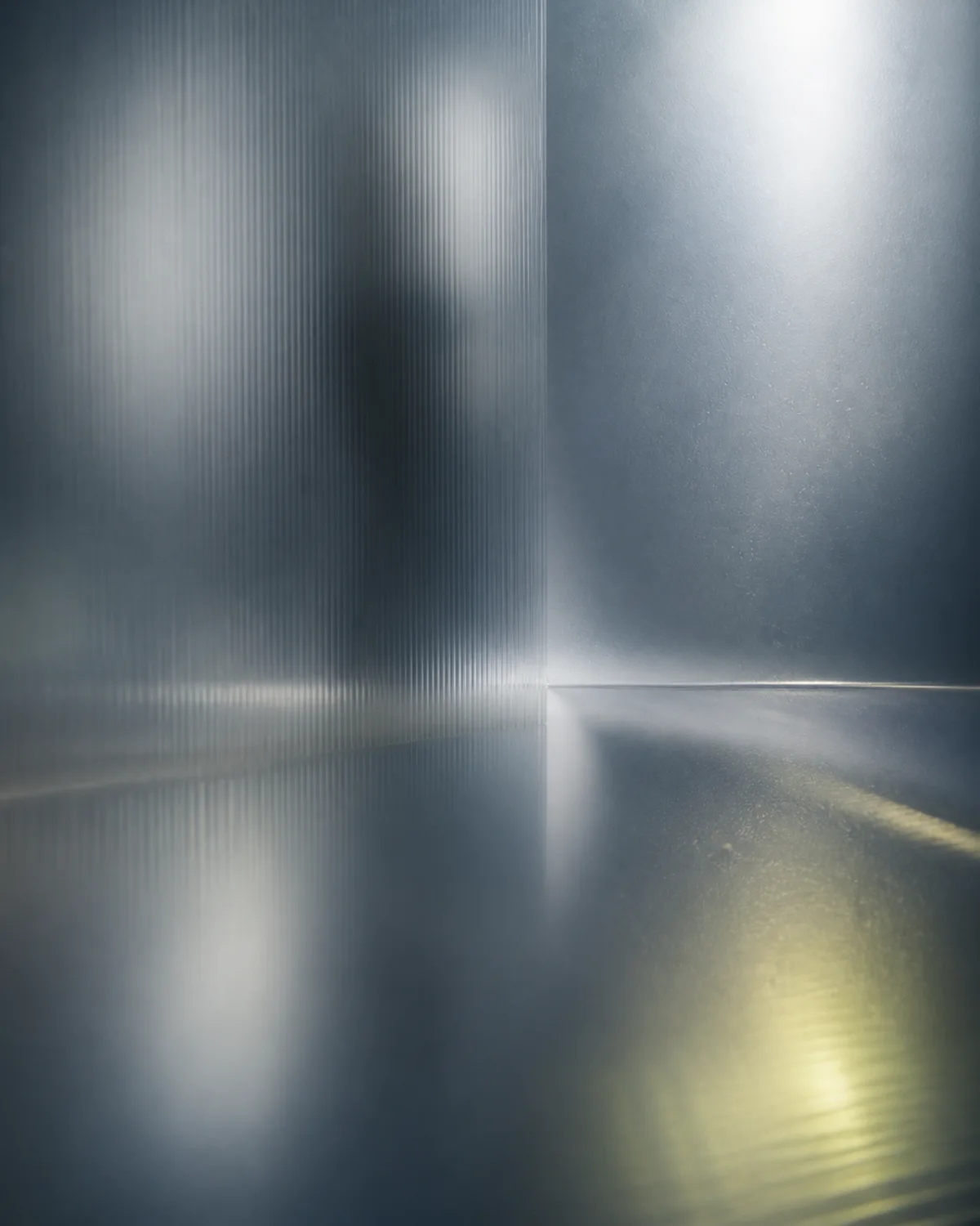 Cool daylight raking across a pane of ribbed glass and a polished steel floor
